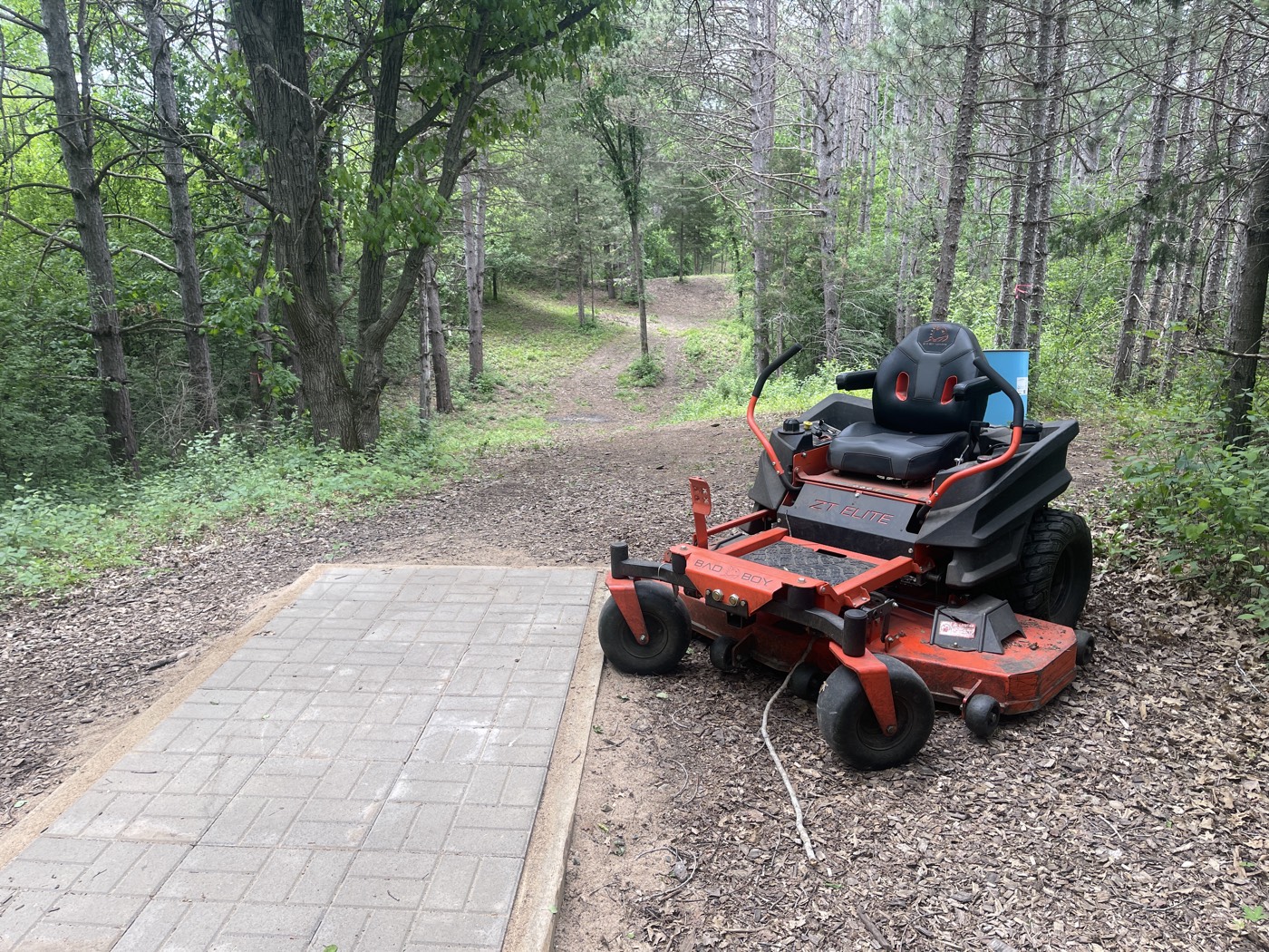 Noah's red zero-turn mower on a wooded trail